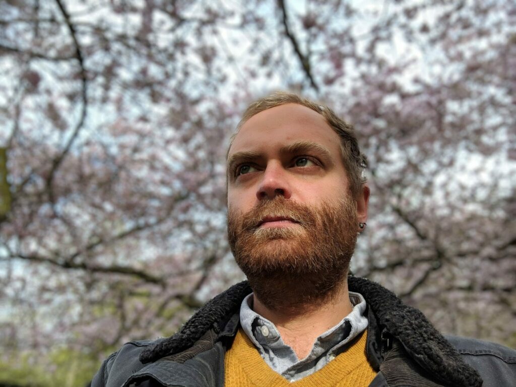 Bearded man looking upward against a backdrop of cherry blossom trees in bloom