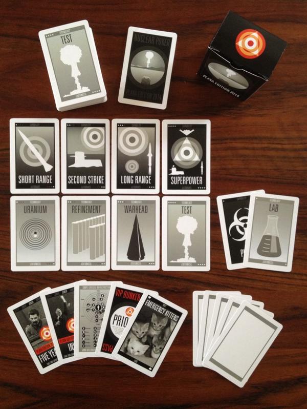 Nuclear-themed card game spread on a wooden table with cards labelled SHORT RANGE, SECOND STRIKE, LONG RANGE, SUPERPOWER, URANIUM, WARHEAD, and a black cube