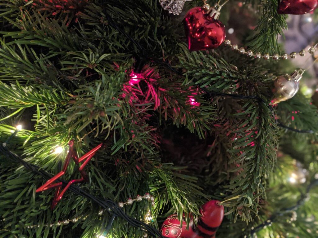 Christmas tree close-up with red ribbon, red and clear baubles, and warm string lights among evergreen branches