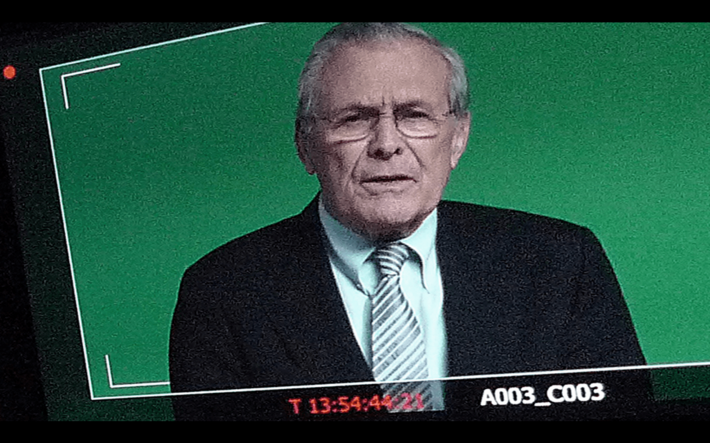 Screenshot of man in suit against green background with timecode and reference code A003_C003