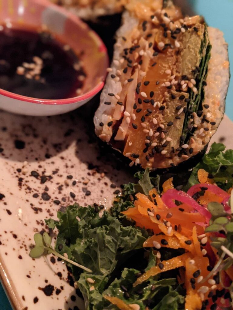 Burger with sesame seed bun, lettuce, and orange toppings on a plate