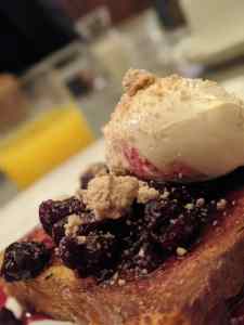Close-up of chocolate brownie with dark jam filling and cream topping, with blurred background