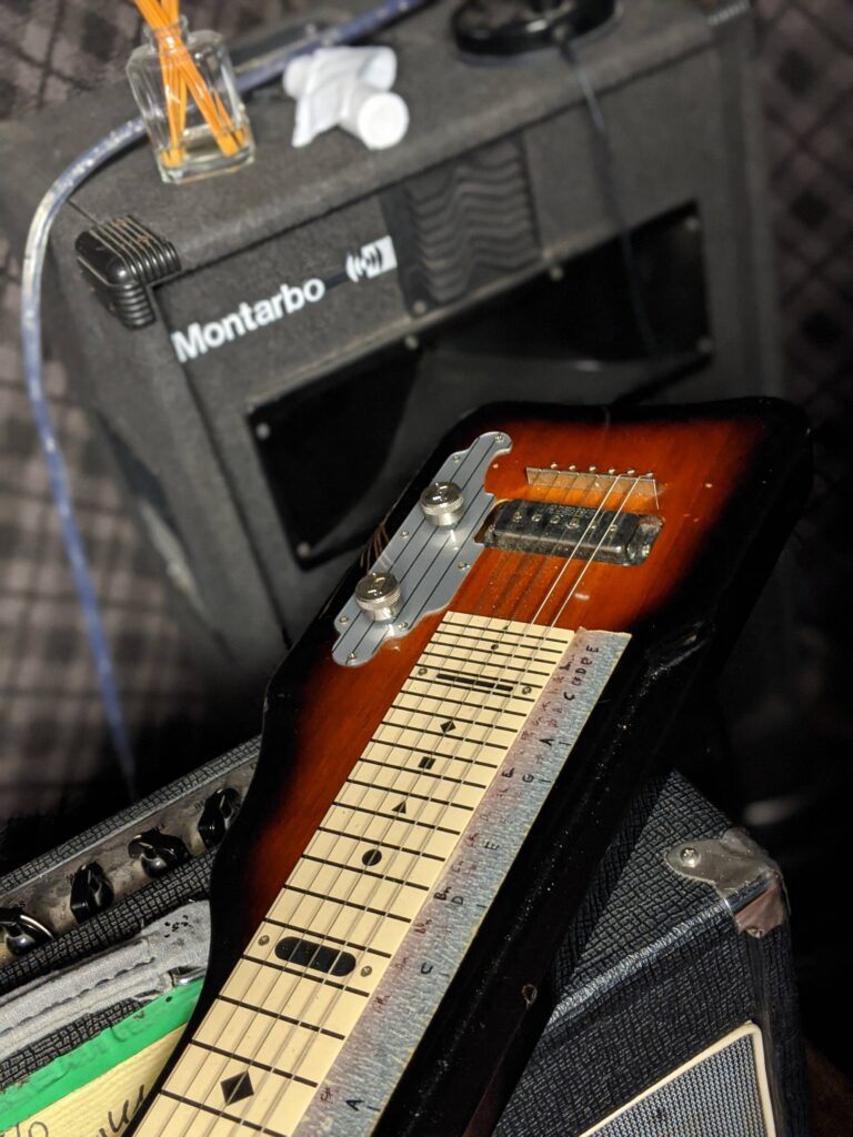 Close-up of sunburst electric guitar leaning against Montarbo amplifier with cables and audio equipment