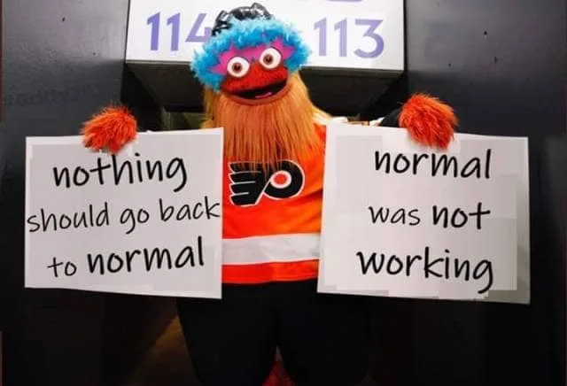 Blue and orange fuzzy character with red hair holding signs that read "nothing should go back to normal" and "normal was not working"