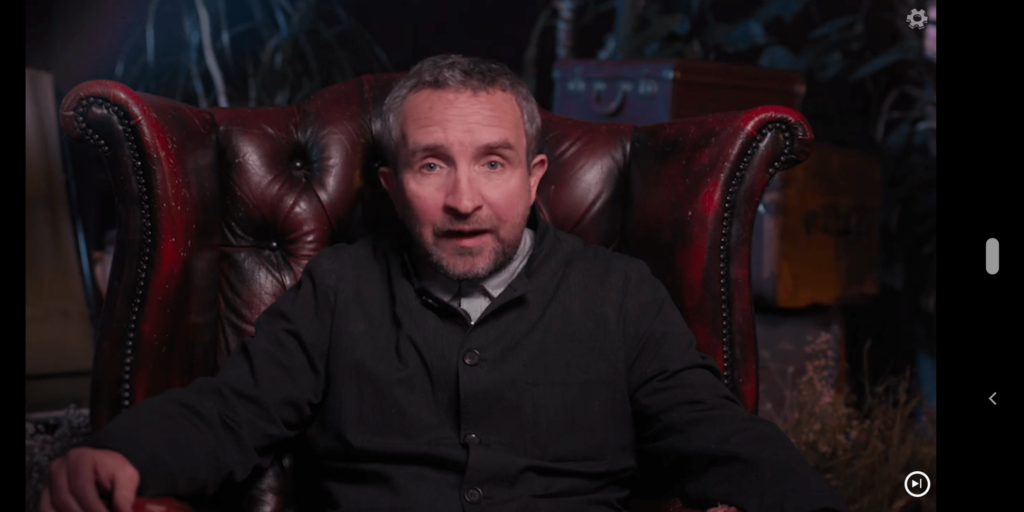 Video screenshot of man sitting in red leather chair in dark interior