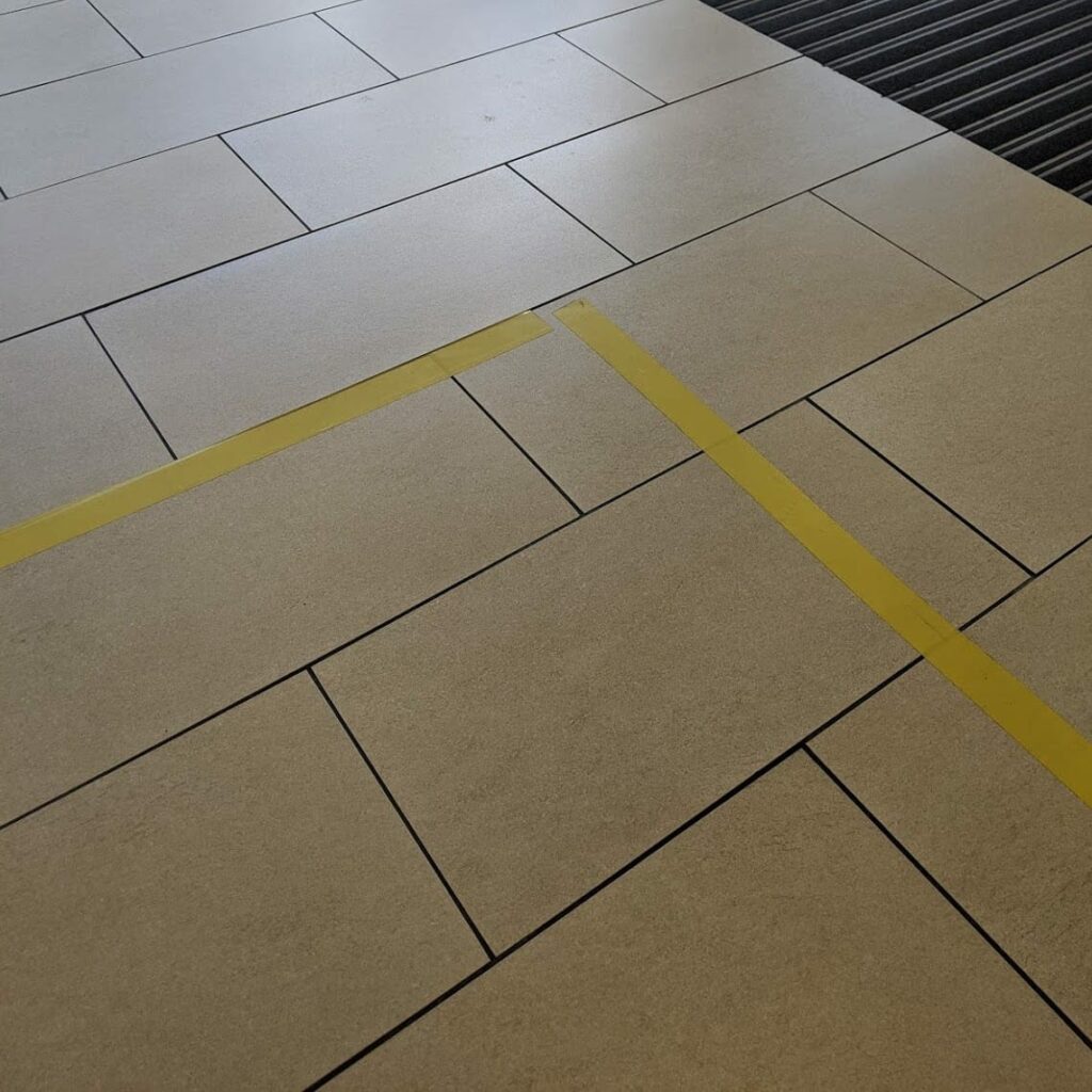 Beige tiles with dark grout lines in herringbone pattern with yellow diagonal stripe
