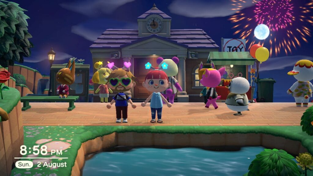 Colorful village scene with animal characters holding balloons and fireworks exploding in night sky above brick buildings