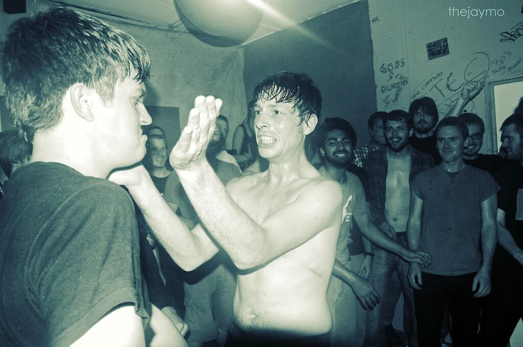 Vintage photograph of men at a hardcore punk show, with several smiling at the camera