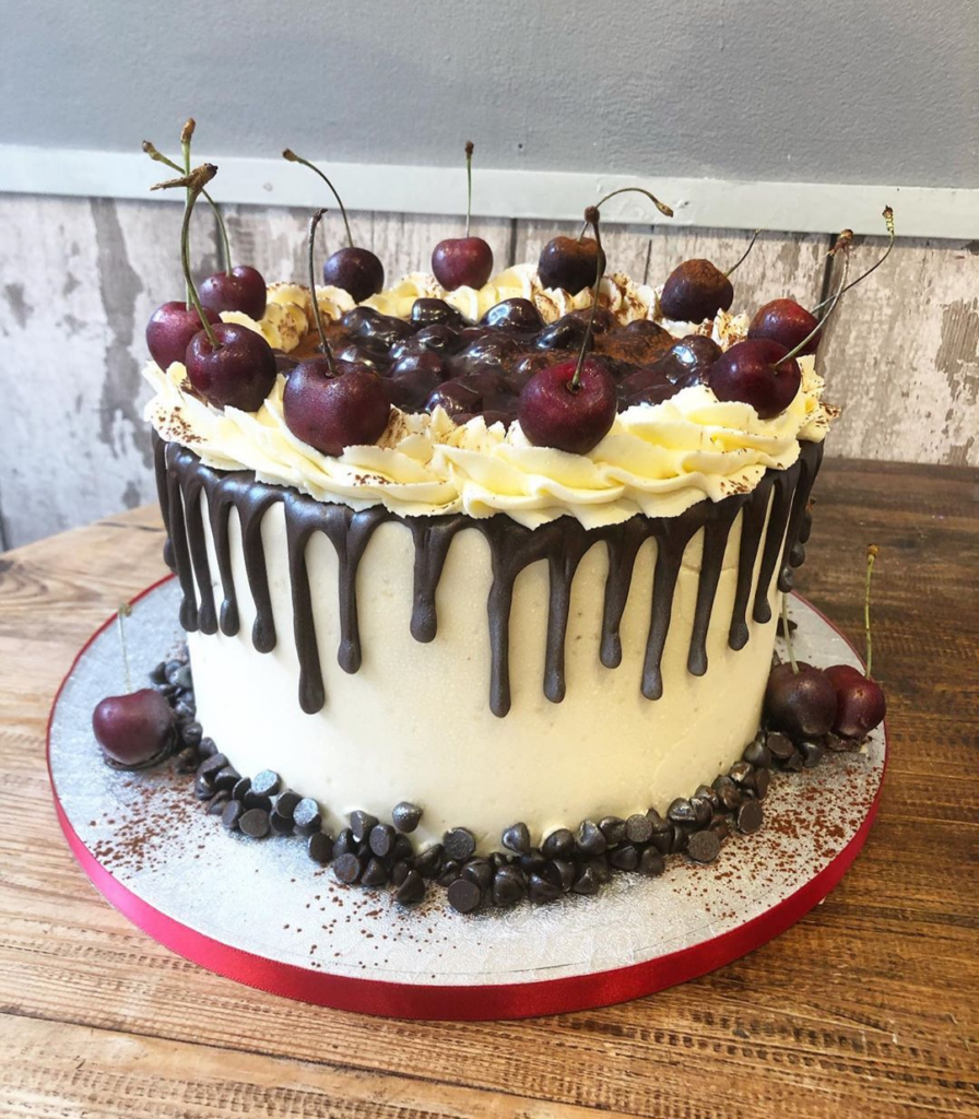 Decorated cake with white frosting, yellow buttercream rosettes, dark chocolate drip, and fresh dark cherries