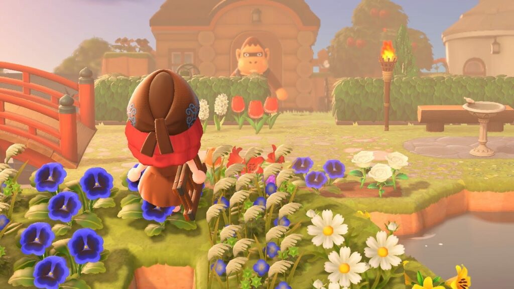 Animal Crossing screenshot of player character viewed from behind in village setting with blue and white flowers, buildings and trees under daytime sky