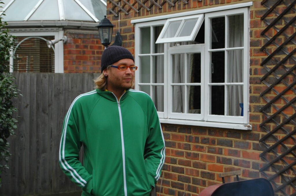 Man wearing green jacket with glasses standing against red brick building with white window