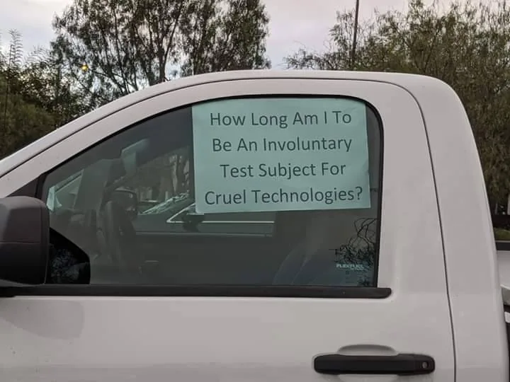 Screenshot of tweet from car window reading "How Long Am I TO Be An Involuntary Test Subject For Cruel Technologies?" trees in background