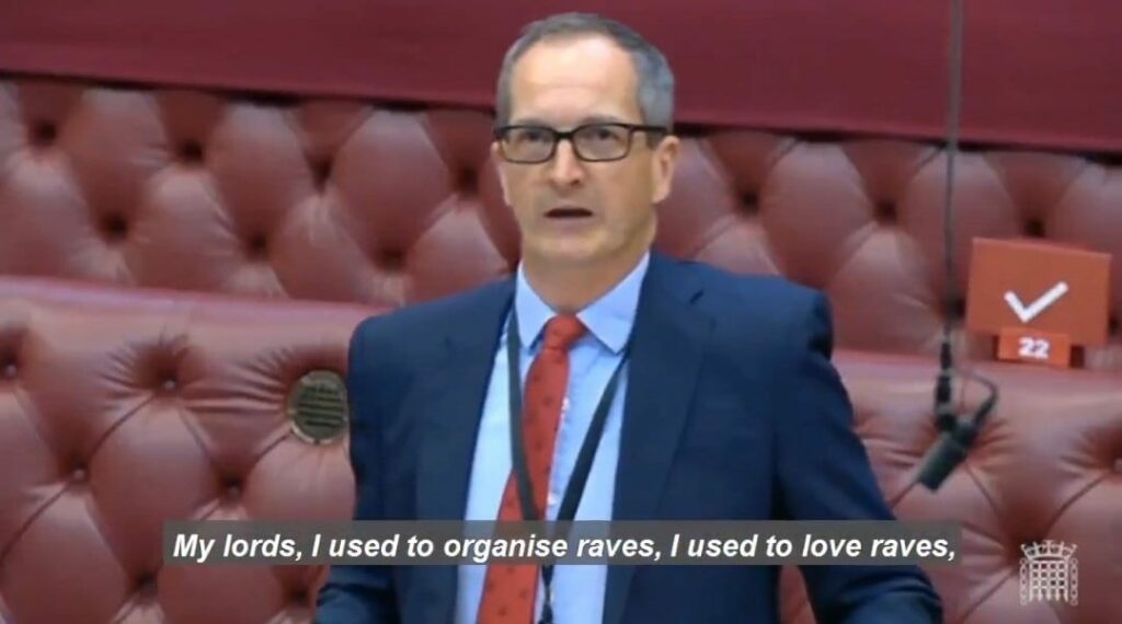 Screenshot of man in blue suit with red tie in parliament chambers with caption about organising raves
