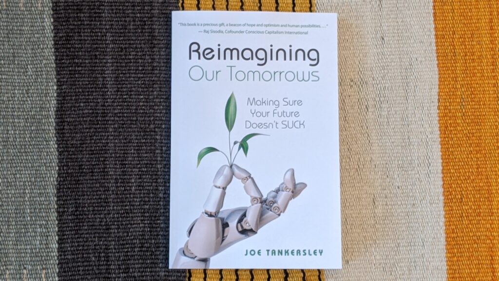 Book cover photo of "Reimagining Our Tomorrows" by Joe Tankersley showing robotic hands holding a plant seedling with striped textile background