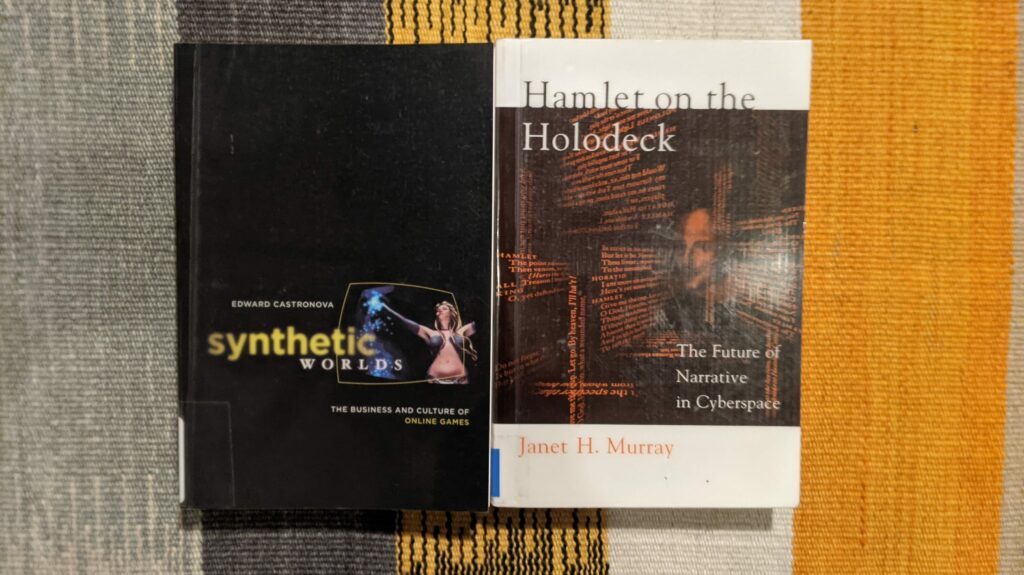 Three books on striped fabric background: Synthetic Worlds, Hamlet on the Holodeck, and a book by Janet H. Murray