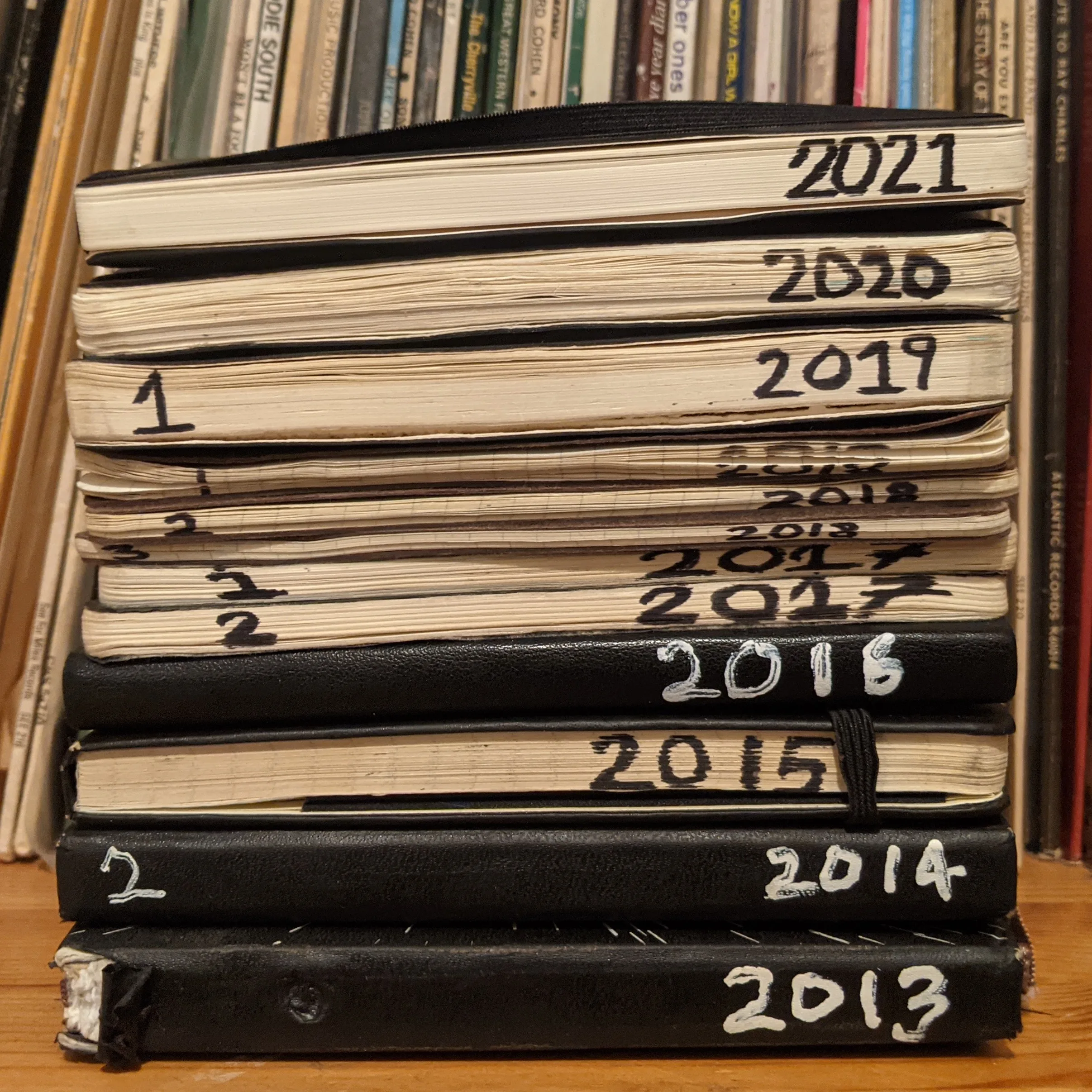 Stack of pocket bullet journals labeled with years 2013 through 2021 against bookshelves