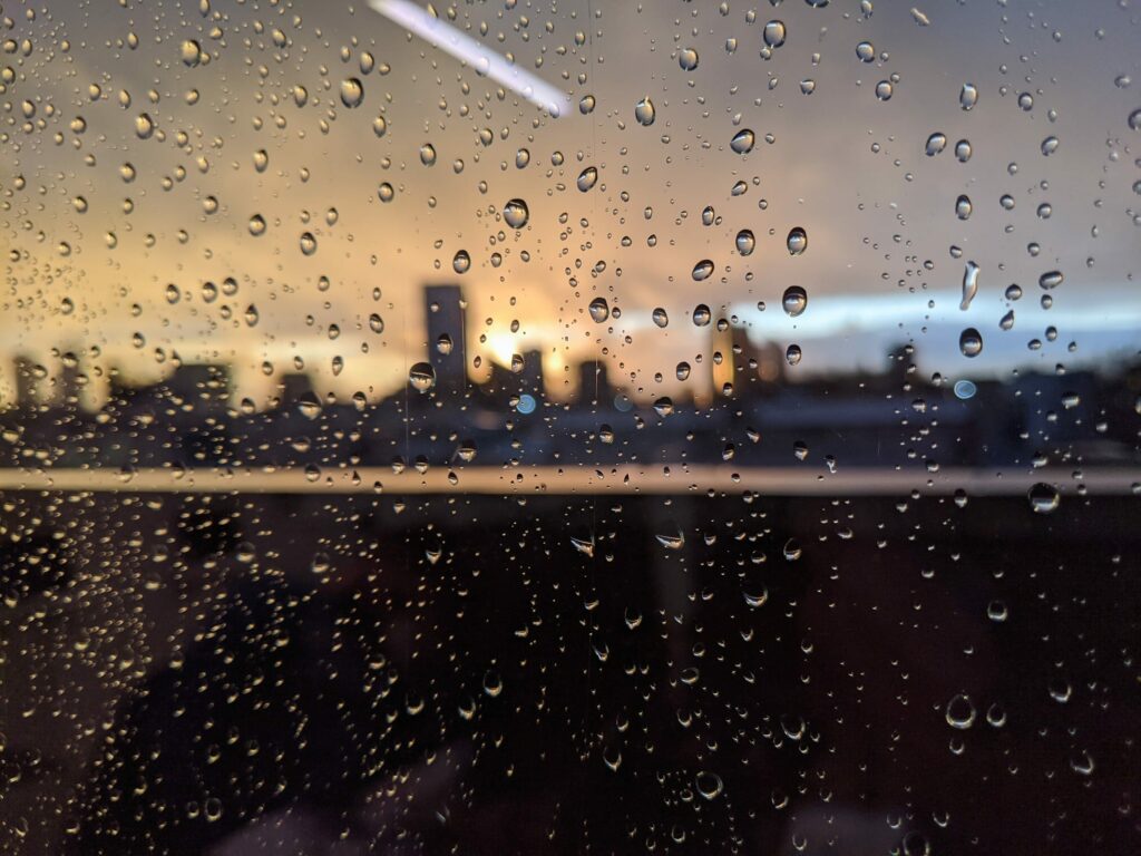 Raindrops on window with cityscape and warm sunset light in background