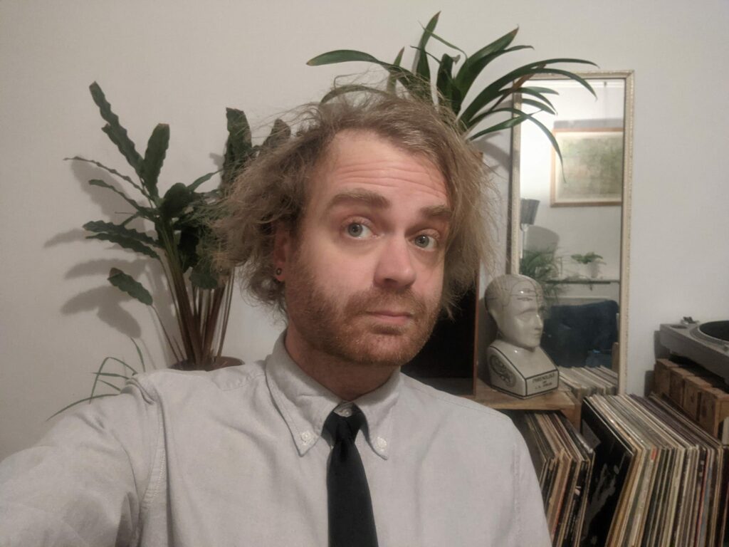 Portrait of man wearing white shirt and black tie with potted plant and shelving in background