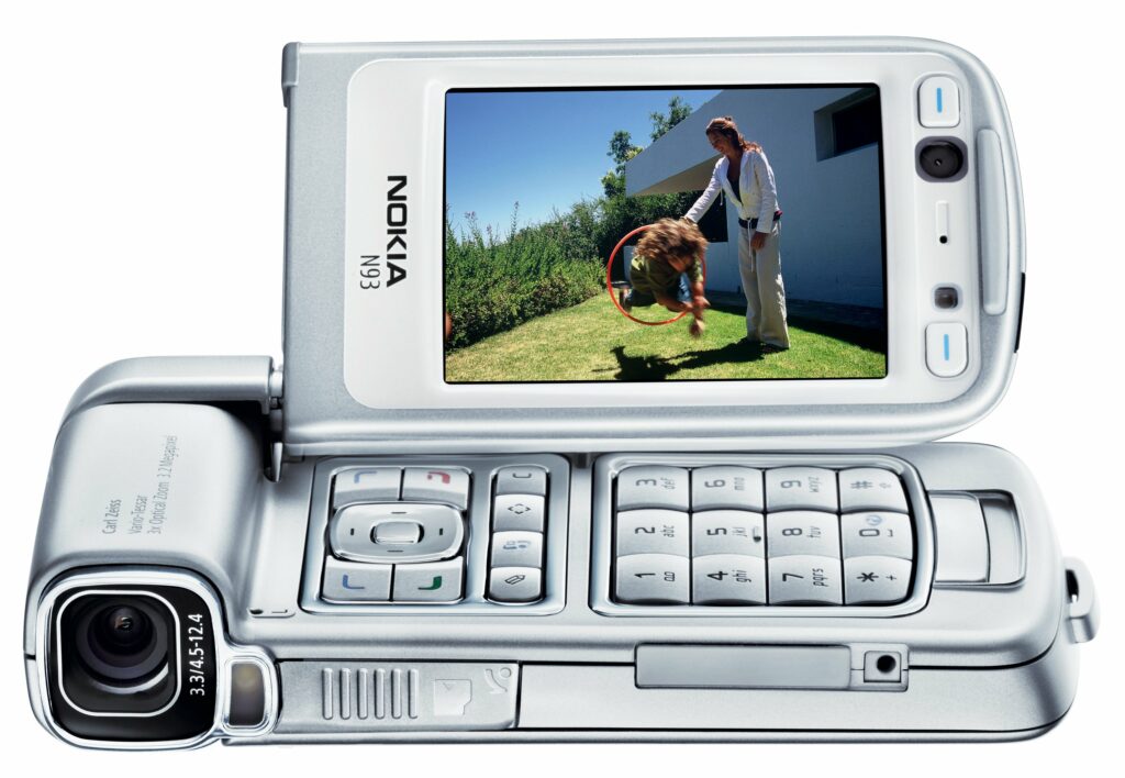 Nokia N93 mobile phone - silver slider phone with screen displaying man and dog on grass, camera lens visible on back