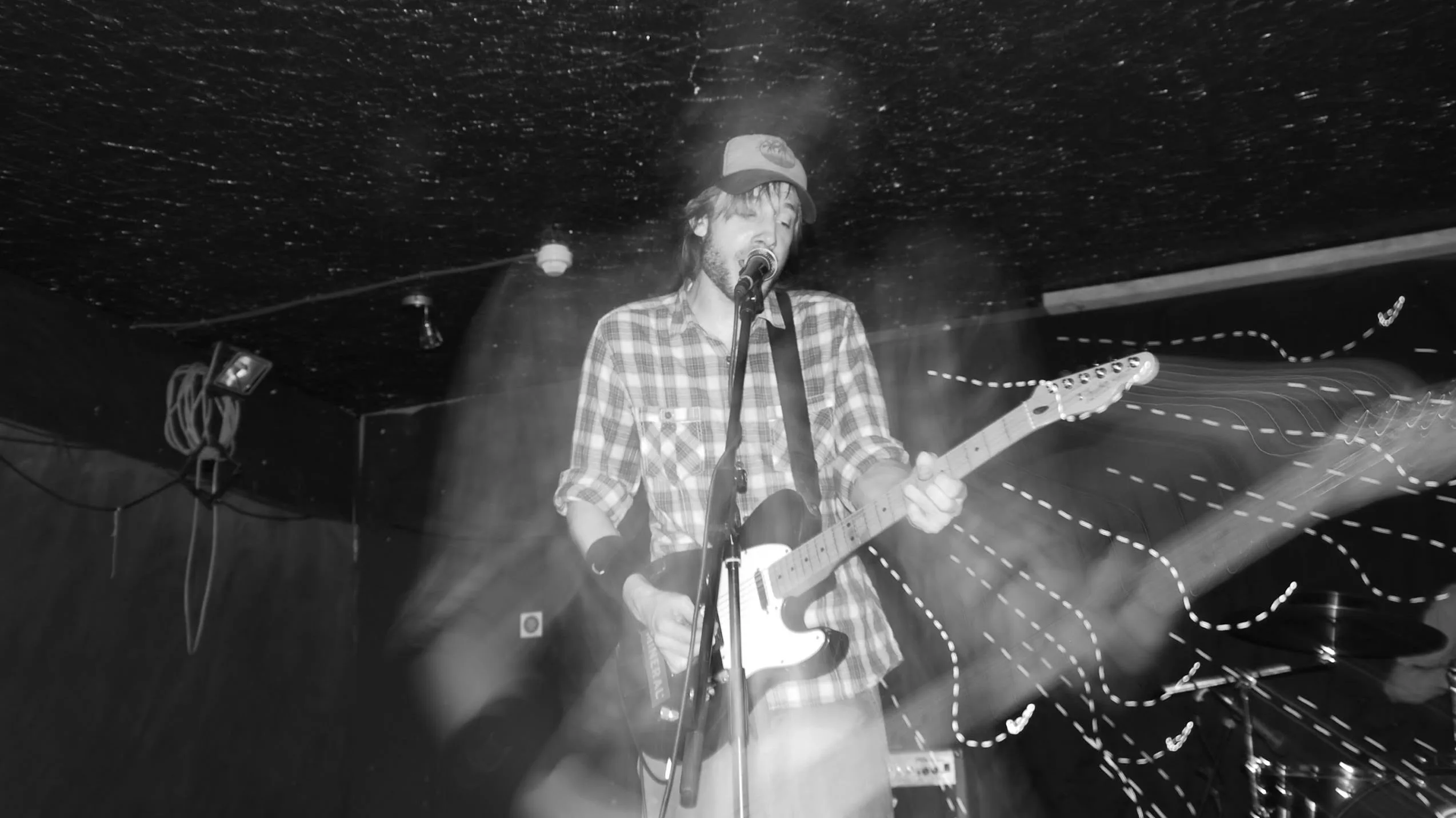 Musician in checkered shirt playing electric guitar on stage during performance, black and white photo