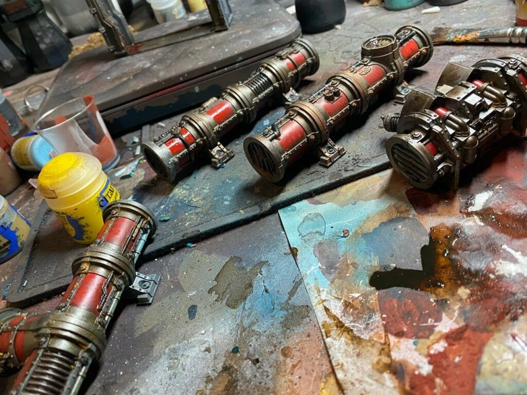 Warhammer 40K weapon components including plasma guns and heavy bolters on weathered base