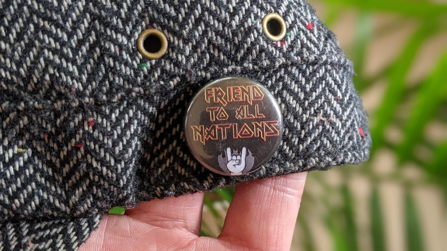 Close-up of Friend to Nations pin on fabric surface with green foliage in background