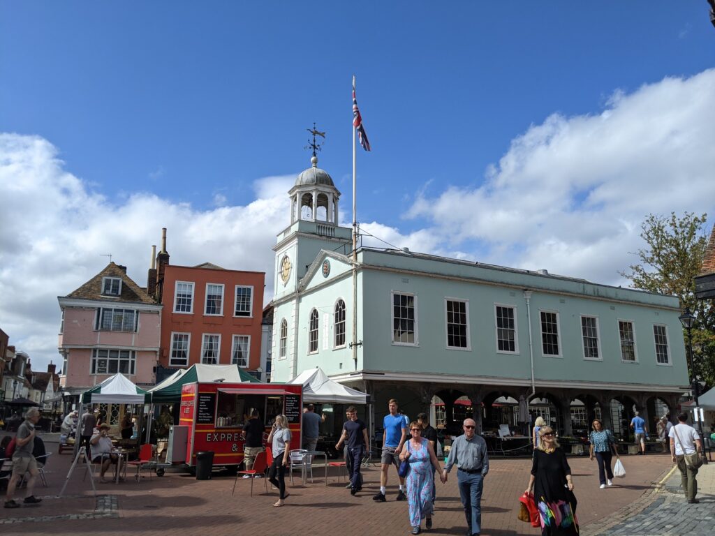 Broadstairs town square with historic white-painted clock tower building with green trim and red brick buildings, outdoor market stalls, pedestrians in summer, blue sky