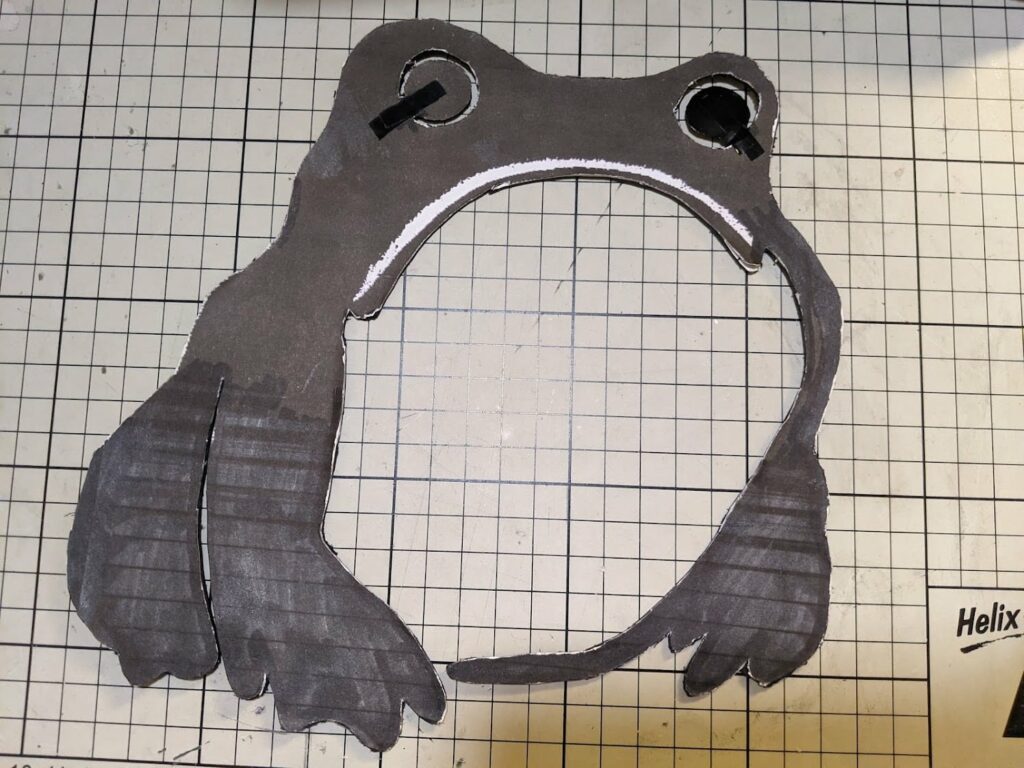 Dark puppet head-shaped fabric with two circular eye holes and white curved smile outline on tiled background