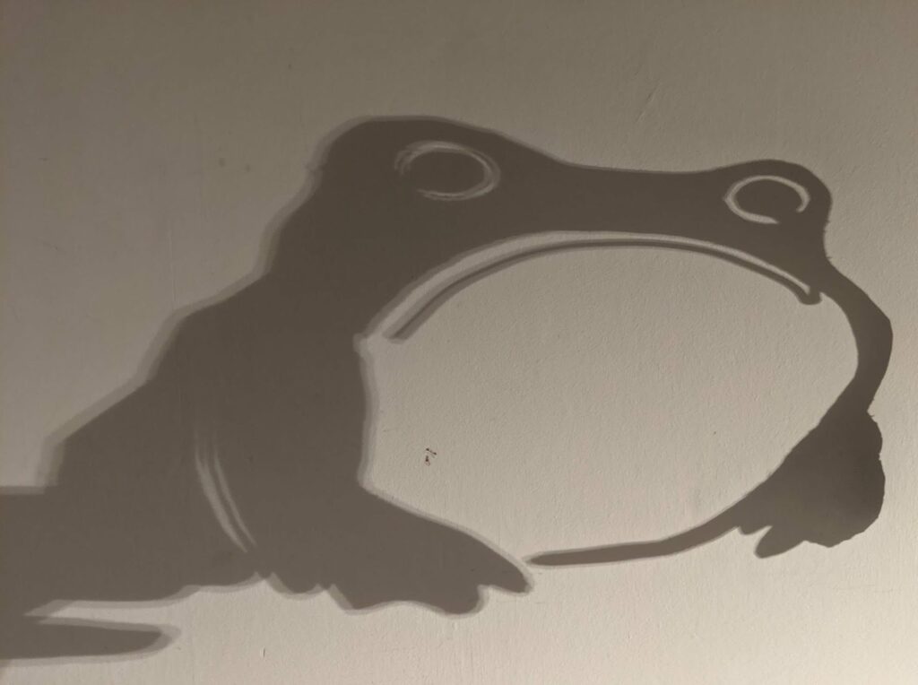 Silhouette of puppet head with two circular eyes and white-outlined mouth against light background