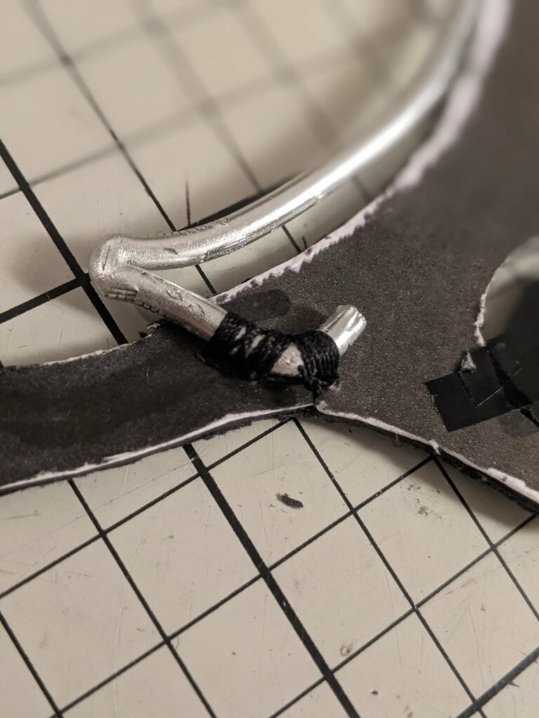 Close-up of puppet armature with metal rods, black wires, dark fabric, and metal joint components on tiled background