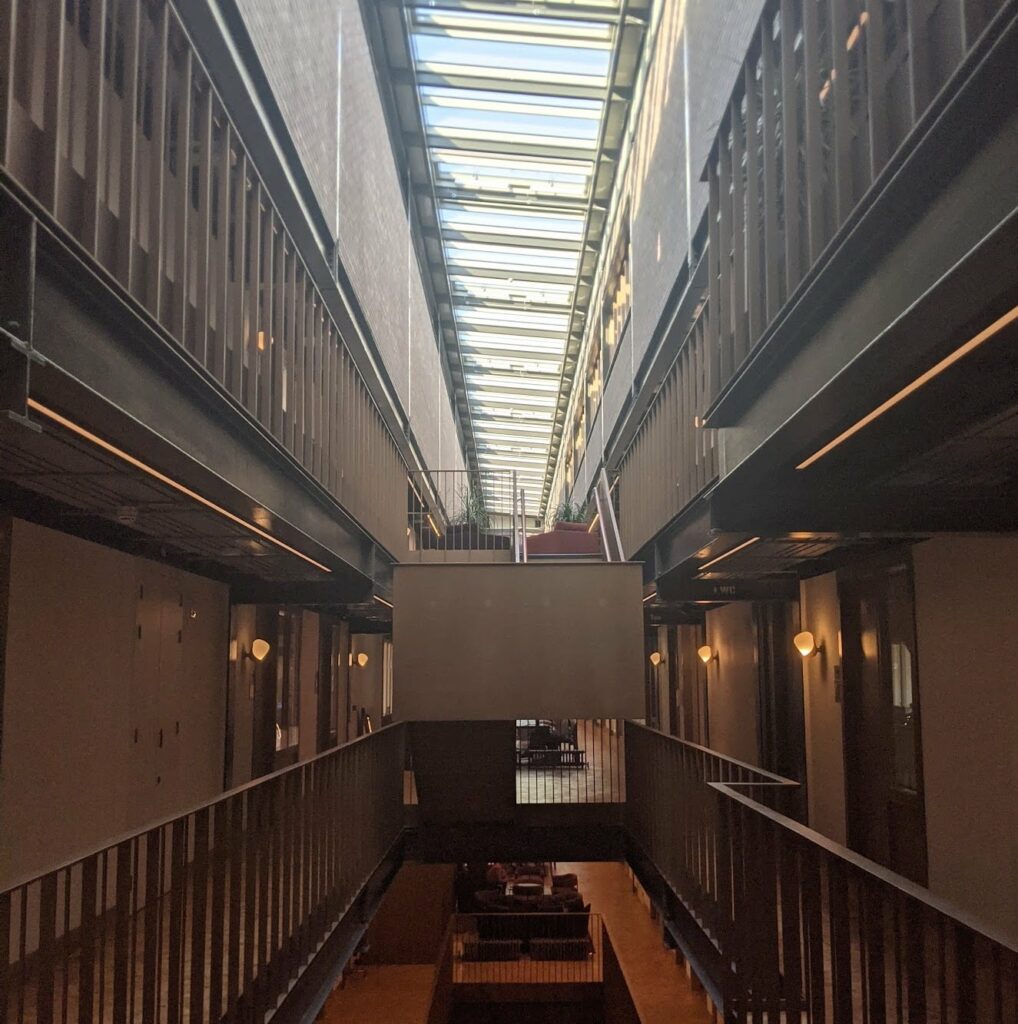 Long industrial corridor with metal railings and skylights running down the center with warm amber lighting