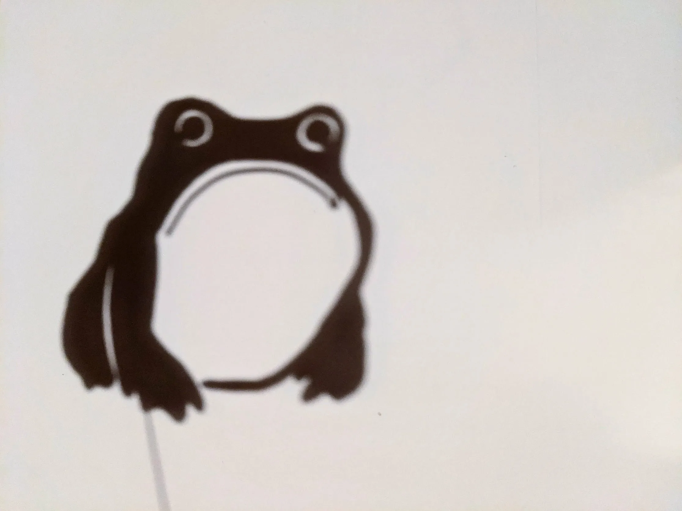 Shadow puppet of a gloomy frog with two circular eyes and large white circular belly on light background