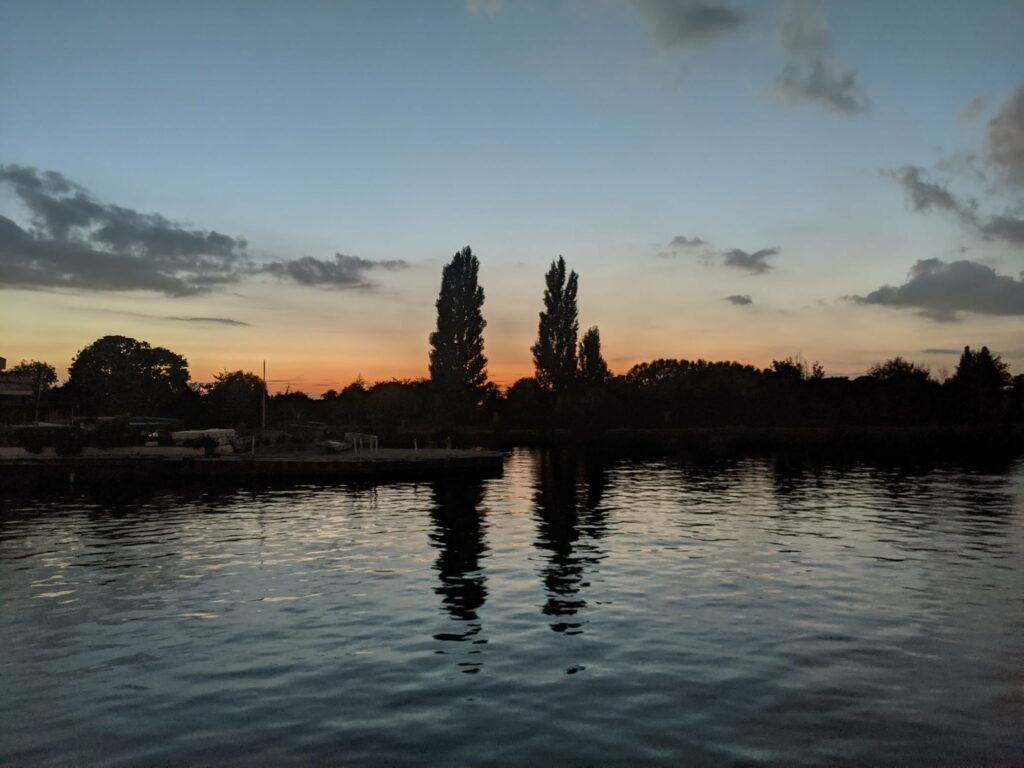 Tall poplar trees reflected in calm water at dusk with orange and blue twilight sky above