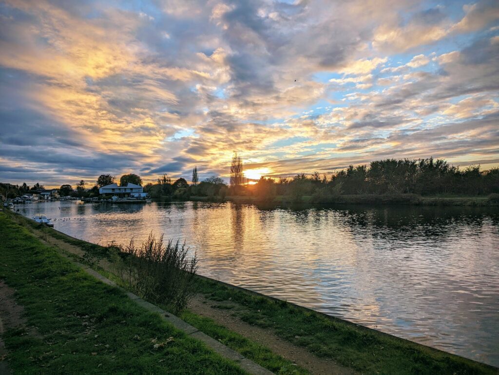 Sunset over the thames with golden and orange clouds reflecting on water, green embankment and trees along shore