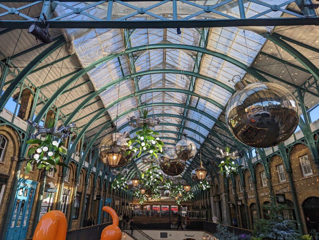 Ornate Victorian glass ceiling and iron framework of Covent Garden market hall with hanging ivy and potted plants