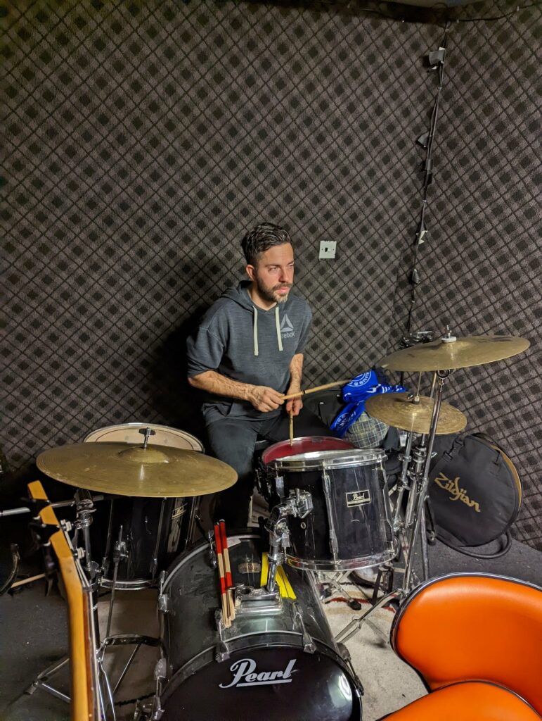 Drummer playing Pearl drums with Zildjian cymbals wearing blue hoodie against textured wall