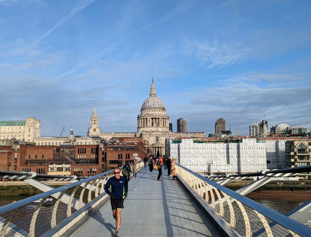 Millennium Bridge in London with runner and pedestrians, St. Paul's Cathedral dome in background across the Thames