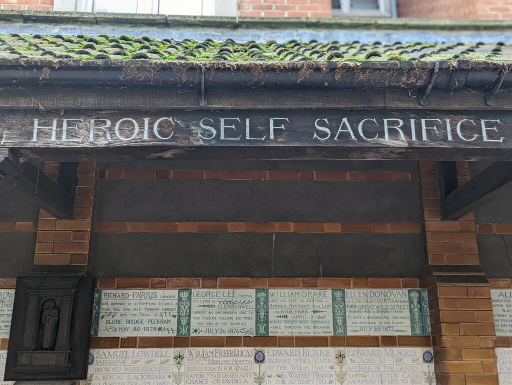 War memorial brick wall with "Heroic Self Sacrifice" text carved in stone and engraved memorial plaques