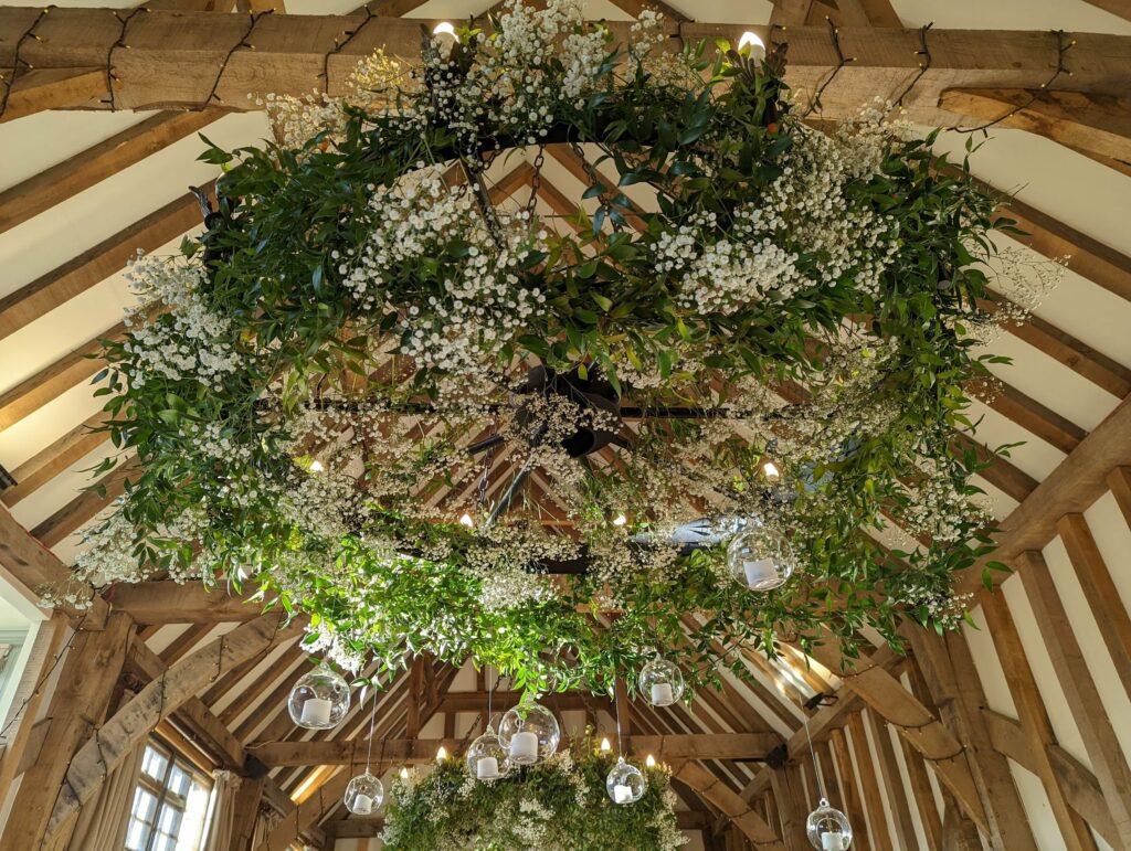Wedding decoration with white baby's breath flowers and green foliage suspended from wooden ceiling beams, hanging glass globes with lights