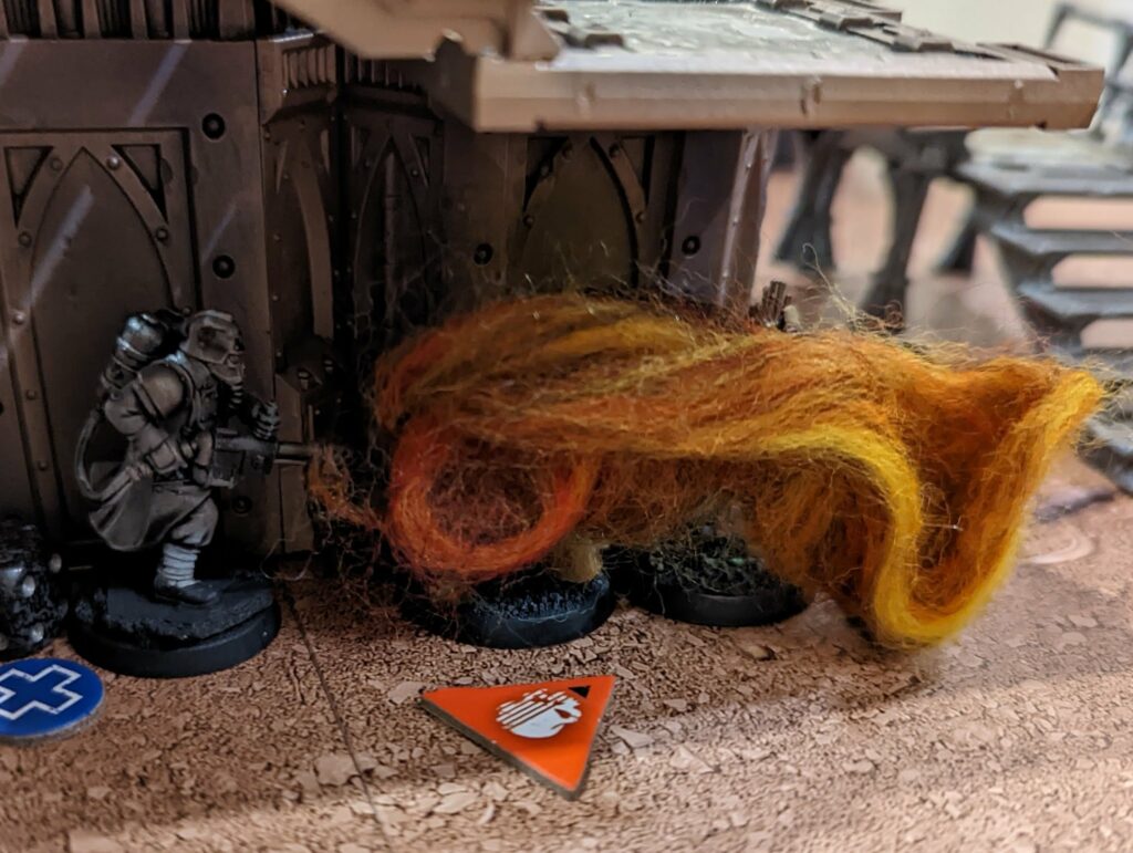 Warhammer 40K miniature with glowing orange and yellow flame aura effect on game board with gothic structures
