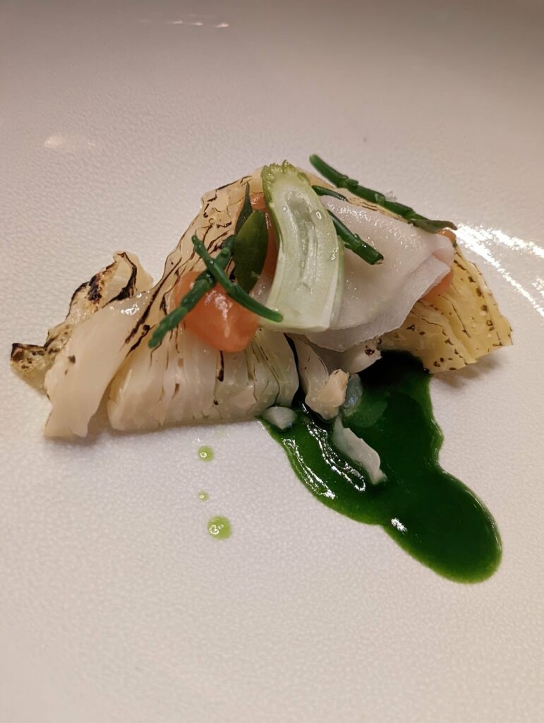 Gourmet cabbage dish with charred edges and herb garnish on green sauce with toast points