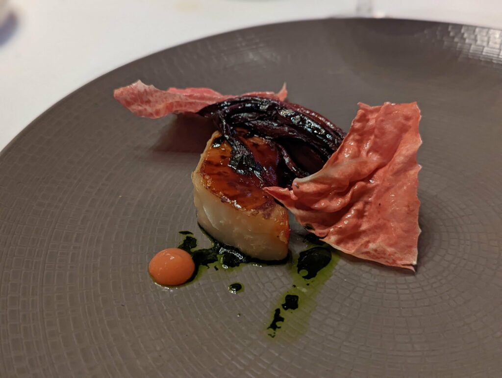 Gourmet leek with seared dark top and crispy beetroot garnish on slate plate with herb oil