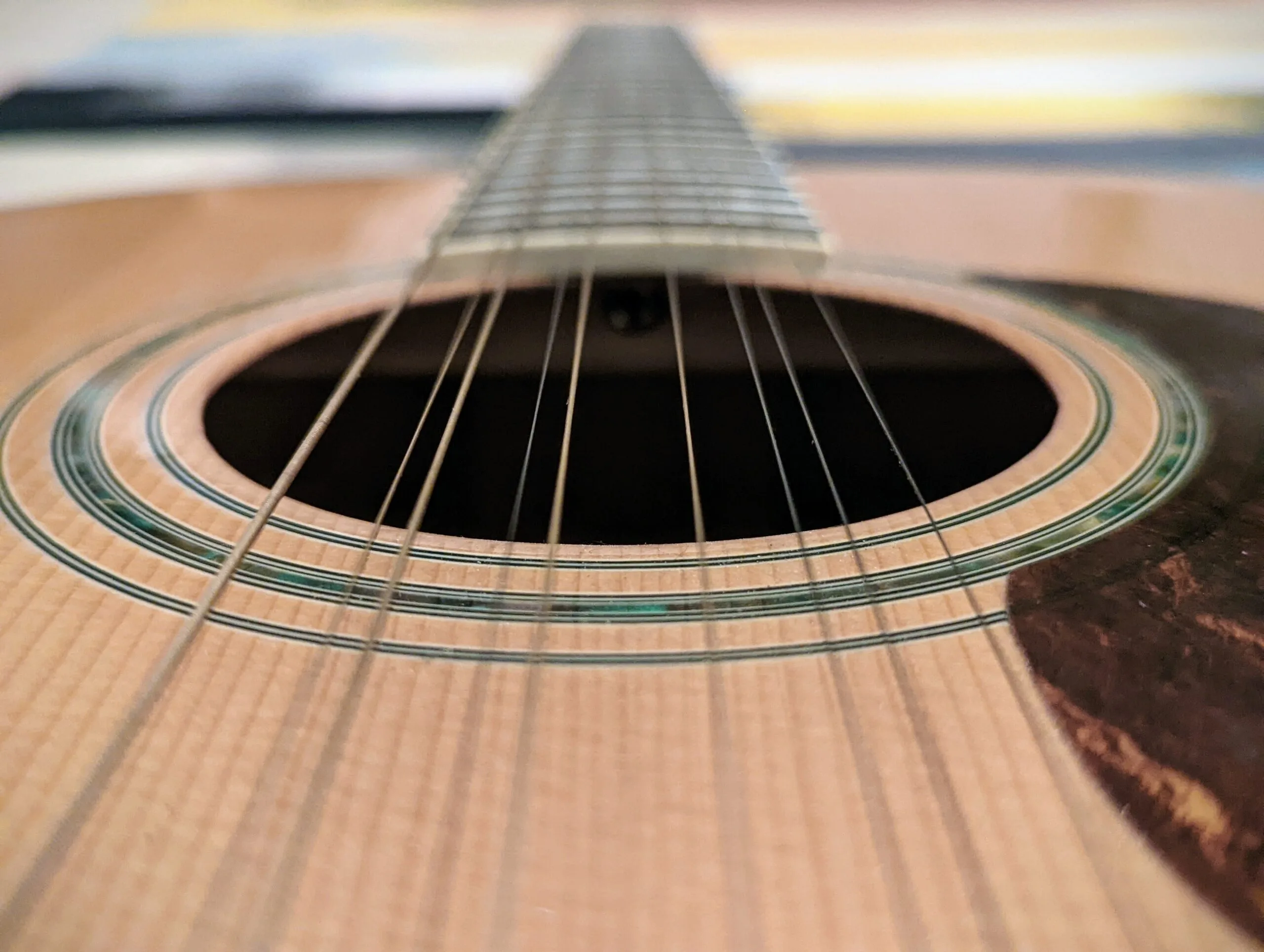Close-up detail of acoustic guitar neck and body with sunset sky and water view in background