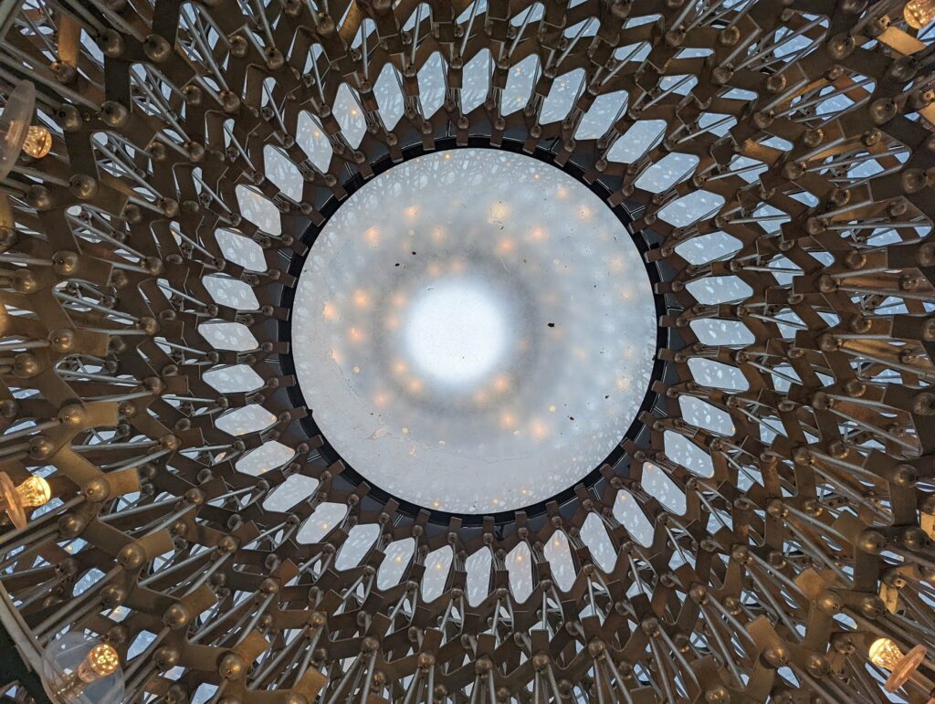 Upward view of domed ceiling with radial skylights and brown wooden beams creating circular pattern