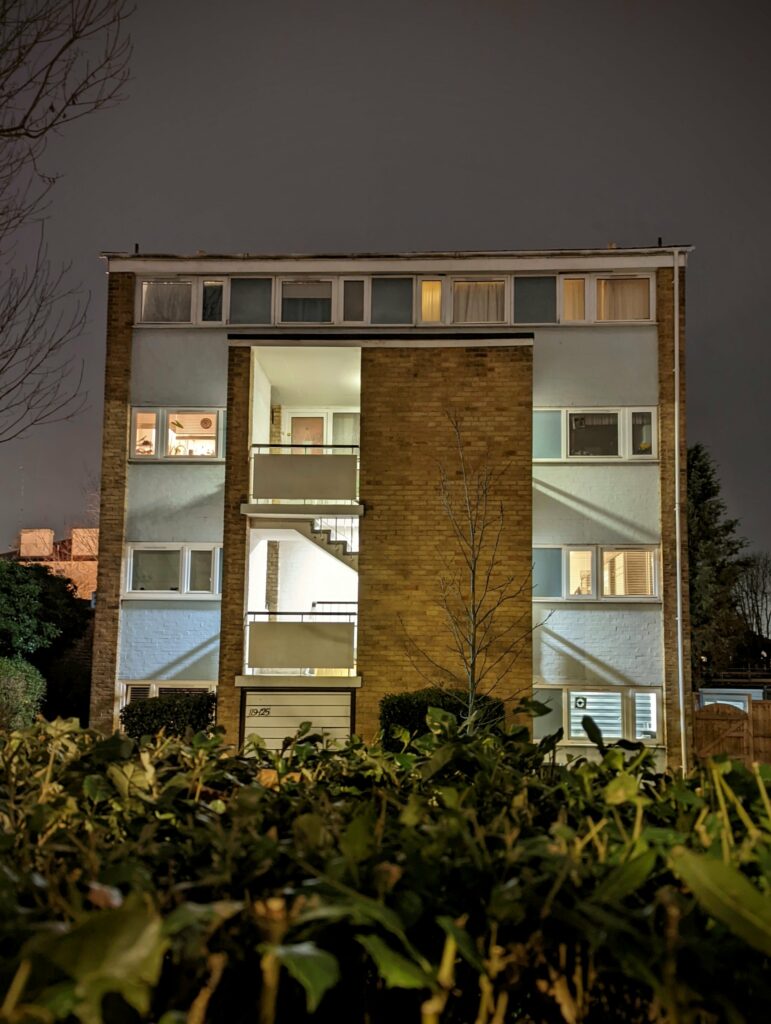 Modern apartment building at night with illuminated windows, brick and pale exterior, dark stormy sky