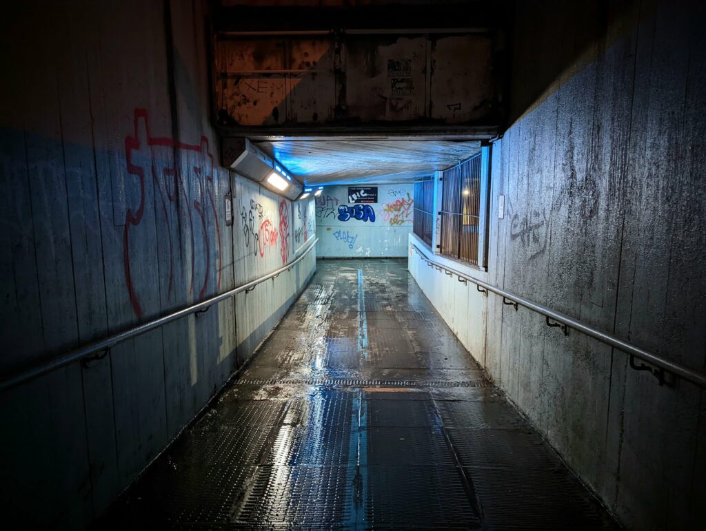 Wet underground pedestrian passage with blue neon ceiling lighting and graffiti on weathered walls
