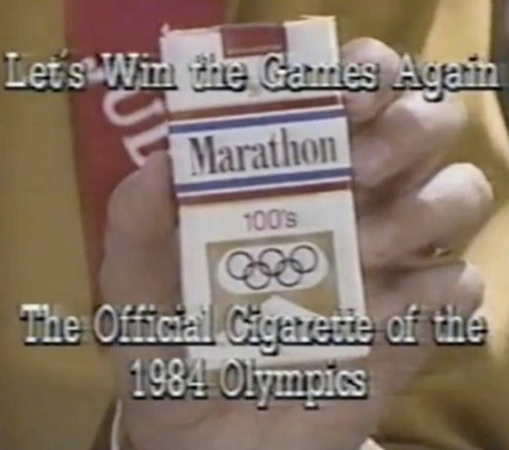 A hand holds Marathon 100's cigarettes. Text: Let's Win the Games Again. The Official Cigarette of the 1984 Olympics.