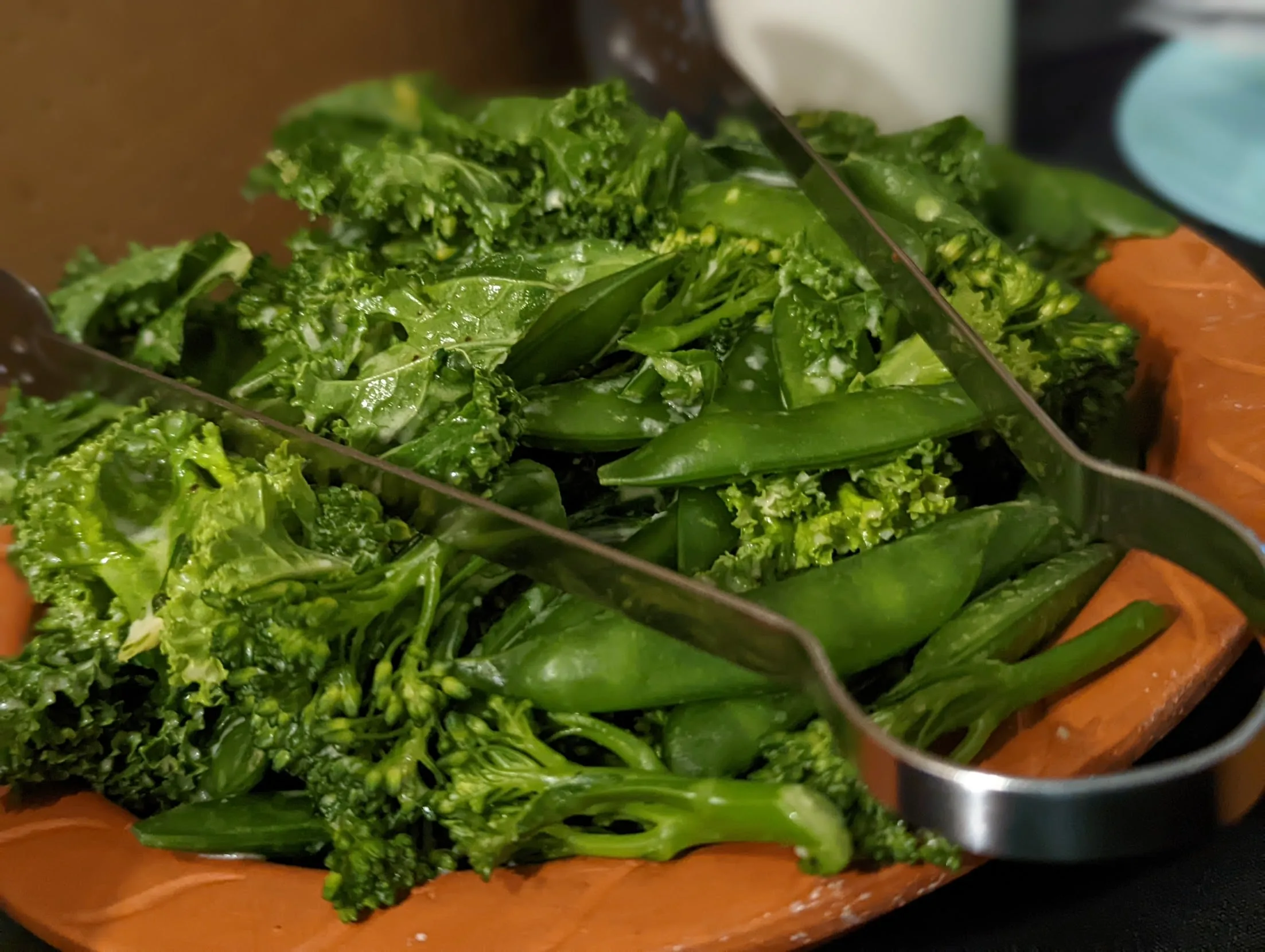 Overhead food photo of cooked kale with peppers in metal serving bowl on wooden board