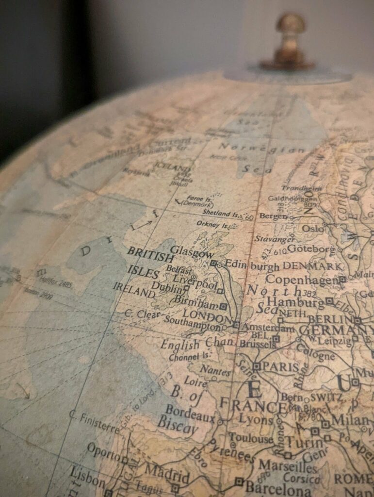 Close-up of a vintage globe featuring Western Europe and the British Isles, with an aged sepia-toned texture and shallow depth of field.