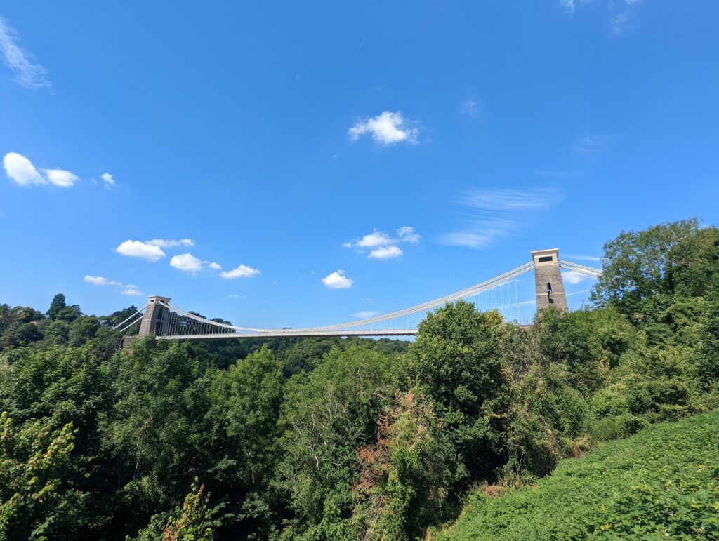 Clifton Suspension Bridge spanning a lush green gorge against a bright blue sky with scattered clouds.